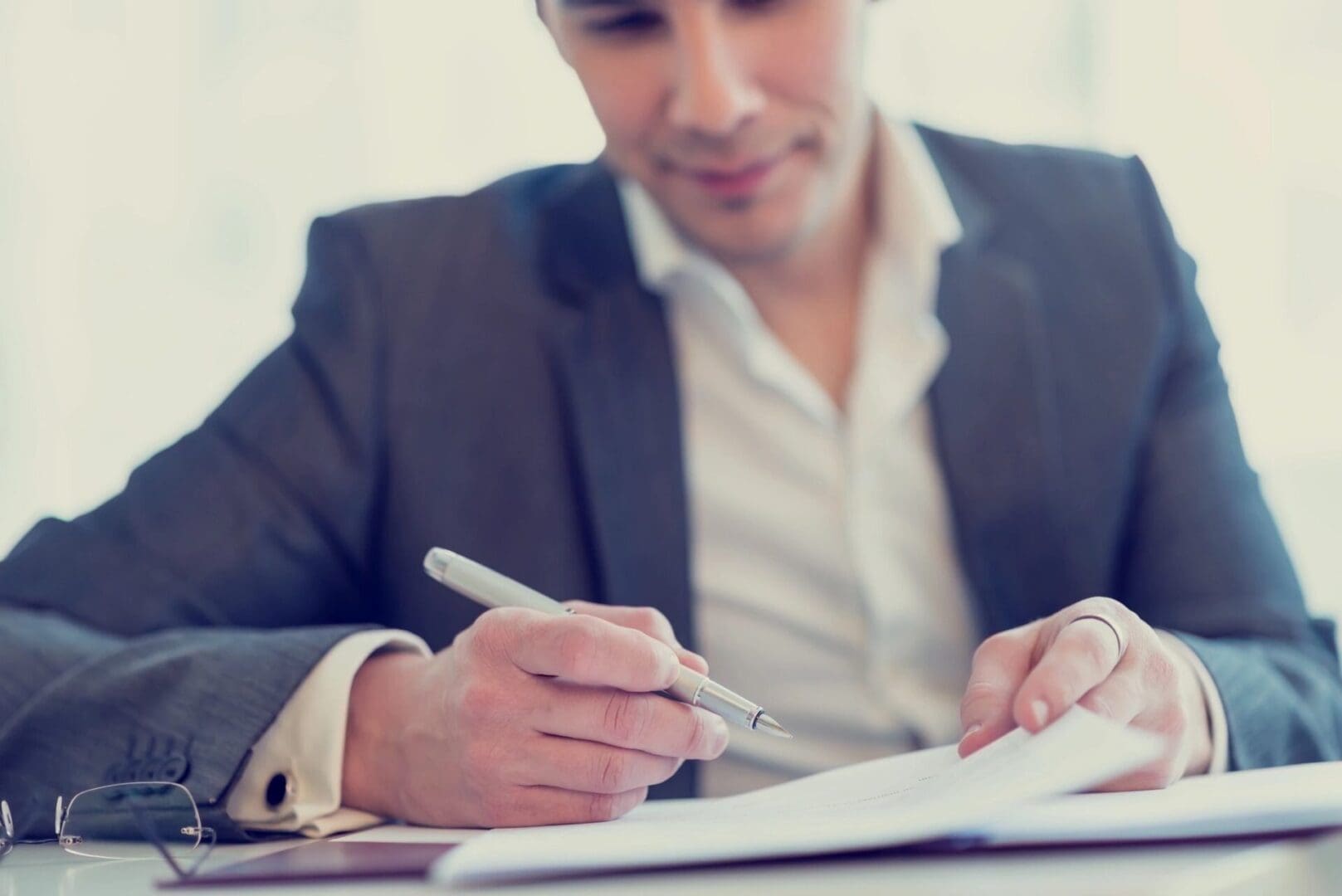 A man in a suit writing on paper with a pen.